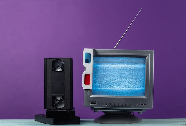 Récepteur de télévision rétro à l'ancienne d'antenne, lunettes 3D anaglyphes et cassettes vidéo sur violet