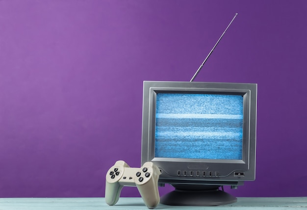 Récepteur de télévision rétro à l'ancienne d'antenne avec manette de jeu sur violet.