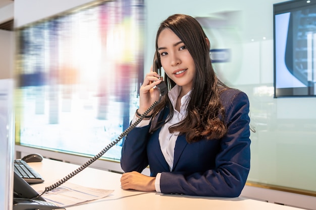 Réception asiatique recevant l'appel au comptoir de la salle d'exposition pour le service au client par téléphone