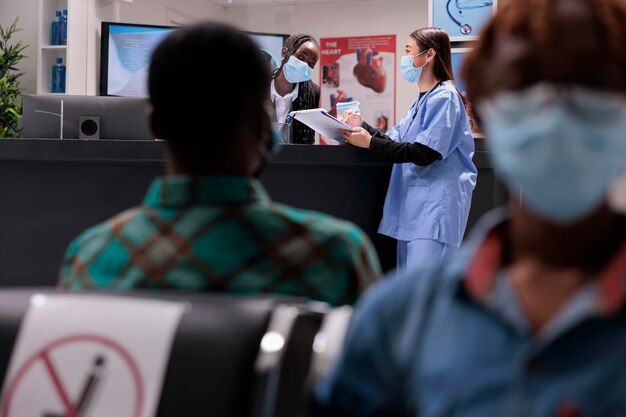 Photo réceptionniste de la clinique féminine parlant à une infirmière asiatique à la réception dans le hall de l'hôpital, discutant des services de santé et des rendez-vous médicaux. personnel de l'établissement pendant l'épidémie de covid 19.