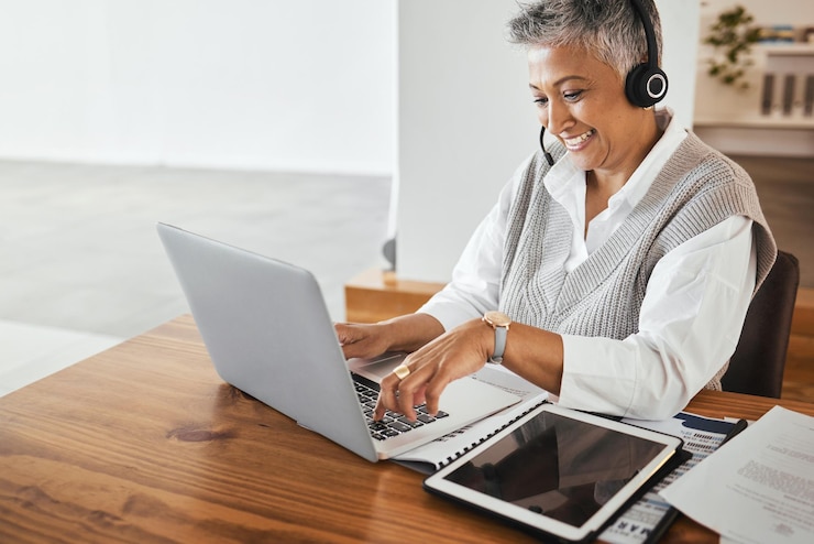 Photo réceptionniste du centre d'appels et consultant senior travaillant sur un casque d'ordinateur portable et une tablette au bureau hotline d'assistance à la clientèle et agent de télémarketing féminin âgé tapant sur un ordinateur sur le lieu de travail