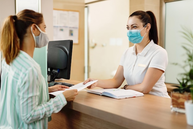 Réceptionniste du spa de santé et son client portant des masques faciaux en raison de la pandémie de coronavirus