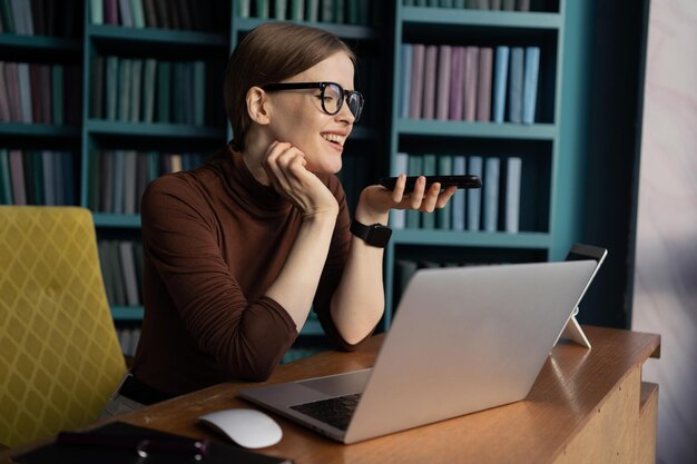 La réceptionniste est une femme à lunettes travaillant dans un bureau moderne à l'aide d'un ordinateur portable