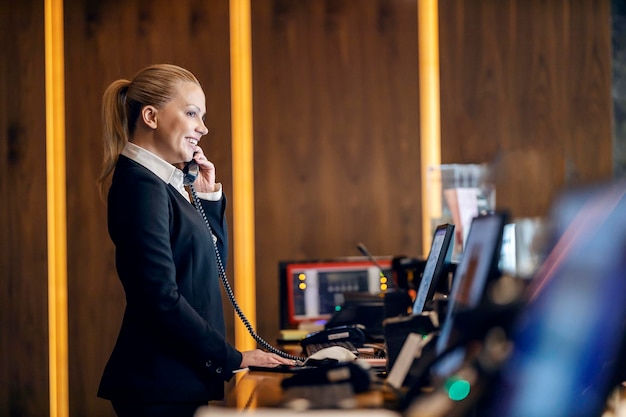 Un réceptionniste heureux parle au téléphone avec un client de l'hôtel tout en se tenant à la réception