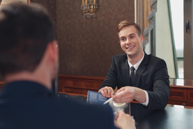 Réceptionniste souriant de l'hôtel aidant l'homme d'affaires à s'enregistrer et à recevoir la clé de la chambre