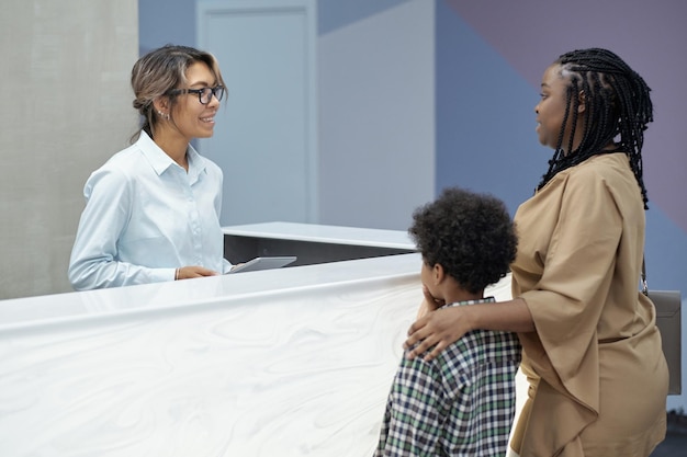 Photo réceptionniste sympathique consultant une jeune femme africaine avec son fils