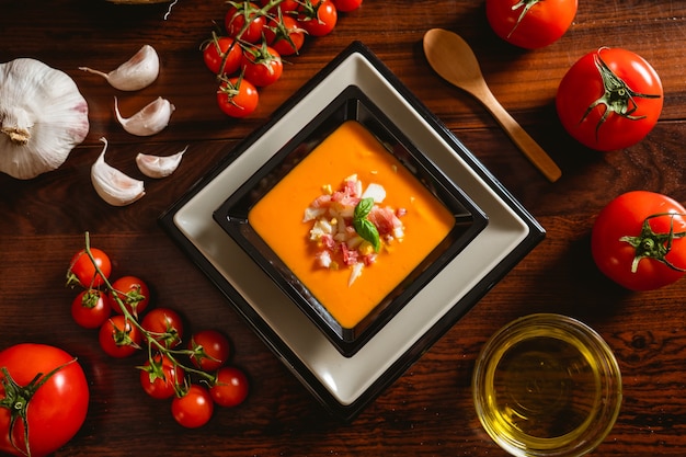 Recette espagnole typique de salmorejo cordovan dans une assiette carrée avec quelques ingrédients autour d'une table en bois.