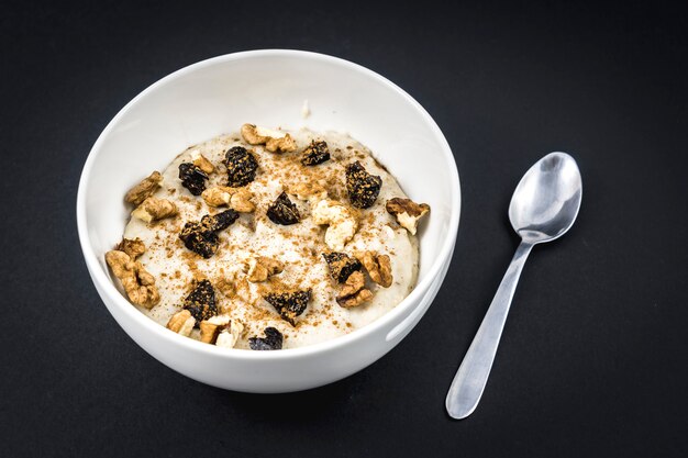 Recette de flocons d'avoine avec noix, prunes, cannelle et sucre préparé pour le petit déjeuner sur fond noir