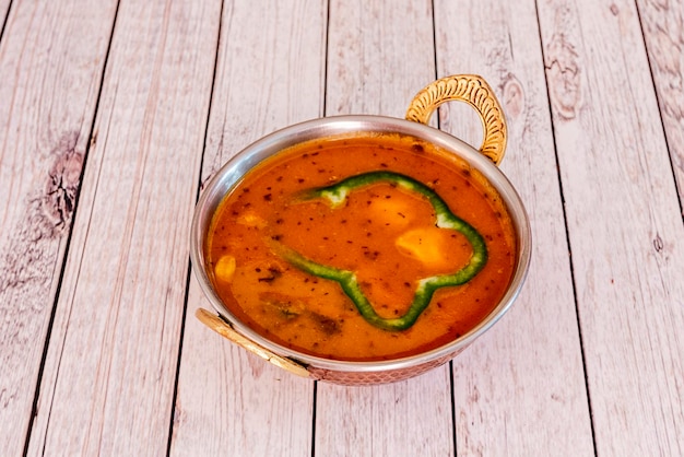 Recette indienne de curry d'agneau présentée dans un bol en métal traditionnel avec poivron et amandes sur une table en bois clair