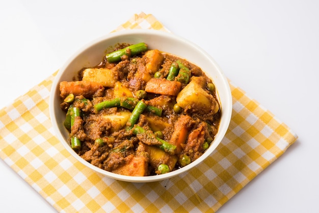 Recette indienne, mélange de légumes contenant des pommes de terre et des haricots avec du masala traditionnel et du curry, rouge chaud et épicé servi dans un bol avec une serviette à carreaux sur une surface blanche