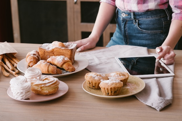 Photo recette en ligne. cuisson de gâteaux et pâtisseries. femelle avec tablette. boulangerie maison sucrée autour.