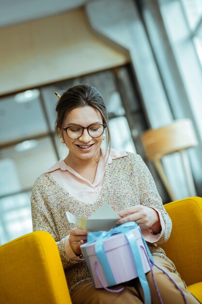 Recevoir un cadeau. Femme d'affaires aux cheveux noirs portant des lunettes recevant un présent au bureau