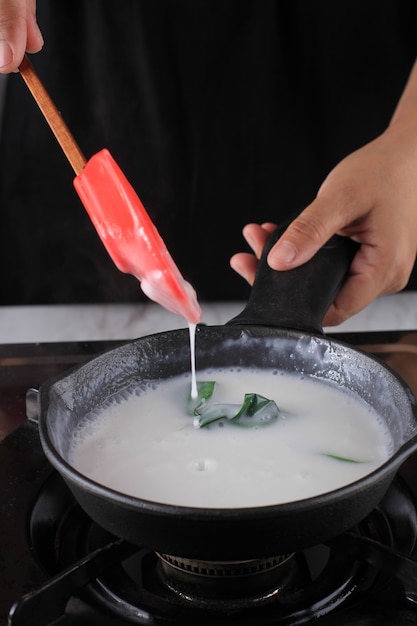 Réchauffer le lait sur une casserole, processus de cuisson faisant de la sauce au lait de coco à l'aide d'une poêle en fonte