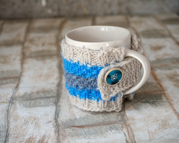 Réchauffeur tricoté sur une tasse de thé avec des boutons de couture à la maison avec des aiguilles à tricoter en gros plan
