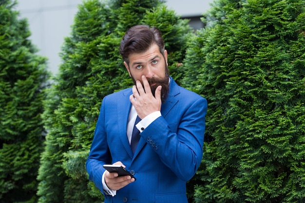 À la recherche d'une grande entreprise agile homme barbu lors d'une réunion d'affaires à l'aide de la technologie moderne look moderne du PDG répondant aux e-mails toujours en ligne homme d'affaires charismatique avec smartphone