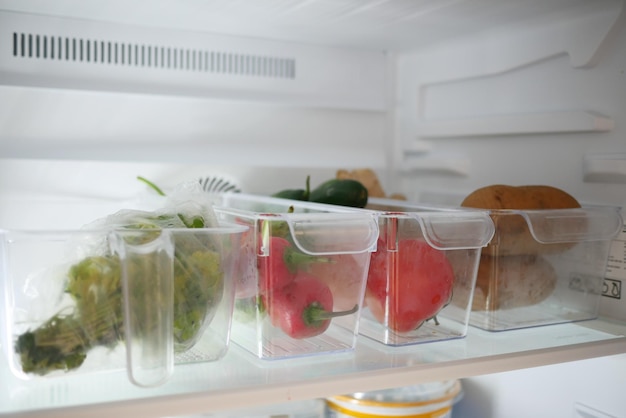 Des récipients en plastique avec différents fruits dans un réfrigérateur ouvert