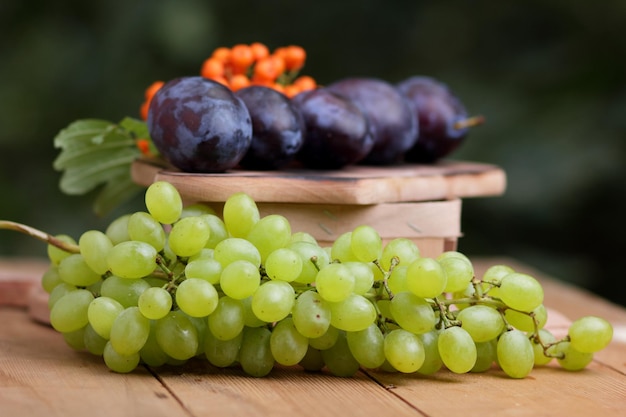 Récolte de fruits crus et biologiques du jardin sur une table en bois Raisins prunes et rowan sur une planche de bois sur un arrière-plan flou