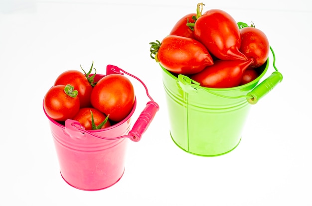 Récolte. Tomates mûres rouges dans des seaux colorés sur fond blanc. Studio photo.