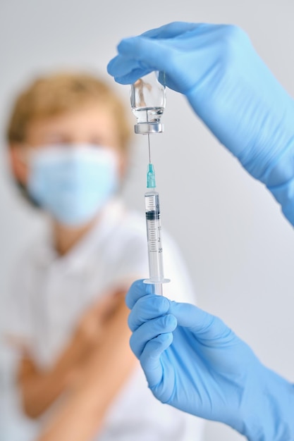 Récoltez un médecin méconnaissable dans des gants stériles avec un petit injecteur de remplissage de bouteille avec le vaccin COVID 19 contre un patient en clinique