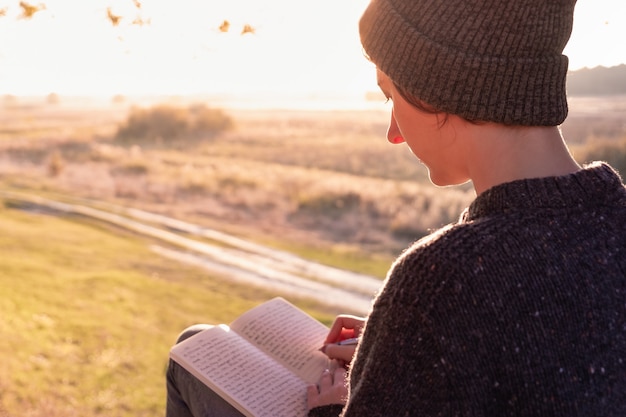 Photo rédaction d'un journal dans une nature magnifique. femme face au soleil du soir prend des notes dans un bloc-notes