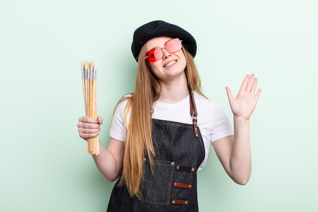 Photo redhair woman smiling joyeusement agitant la main vous accueillant et vous saluant concept d'artiste