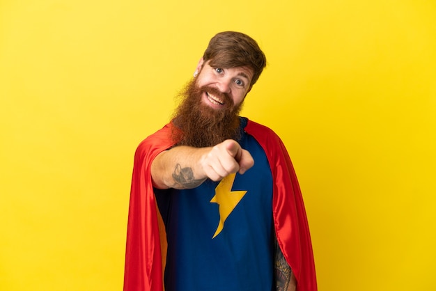 Redhead Super Hero man isolé sur fond jaune pointe le doigt vers vous avec une expression confiante