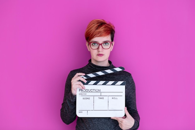 redhead woman holding movie clapper isolé sur fond rose concept de cinéma en studio