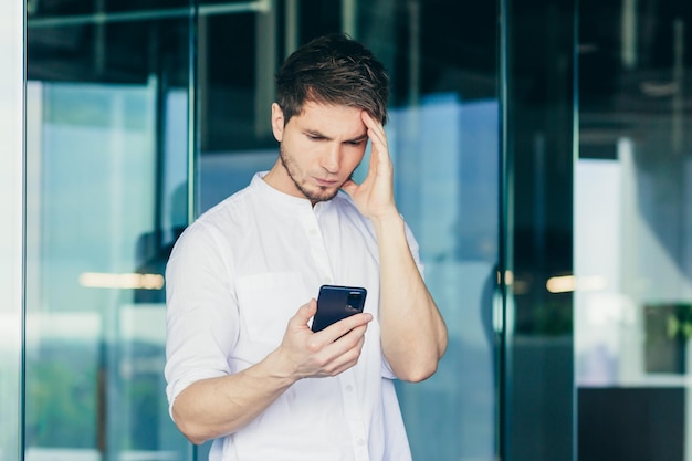 Réfléchi et inquiet jeune homme d'affaires indépendant homme d'affaires regarde le téléphone tient sa tête a reçu de mauvaises nouvelles