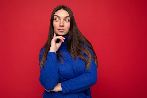 Réfléchi jeune belle femme brune avec des émotions sincères isolées sur le mur du mur avec espace copie portant un pull bleu à la mode décontracté. Concept de pensées.