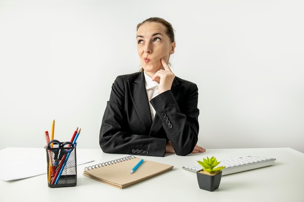 Réfléchi jeune femme en veste assis à table sur le lieu de travail