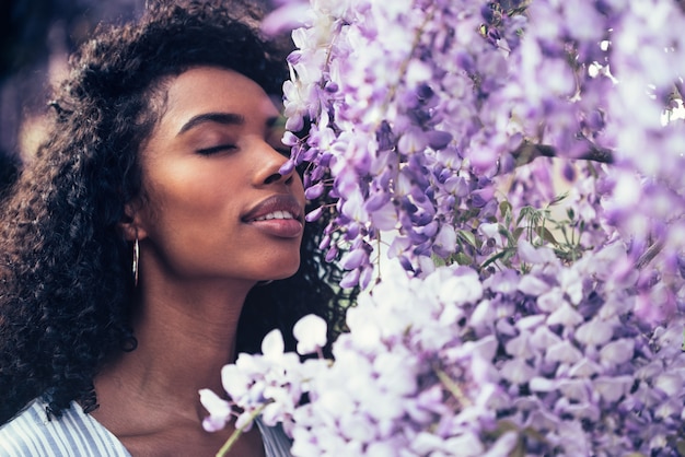 Réfléchie heureuse jeune femme noire entourée de fleurs