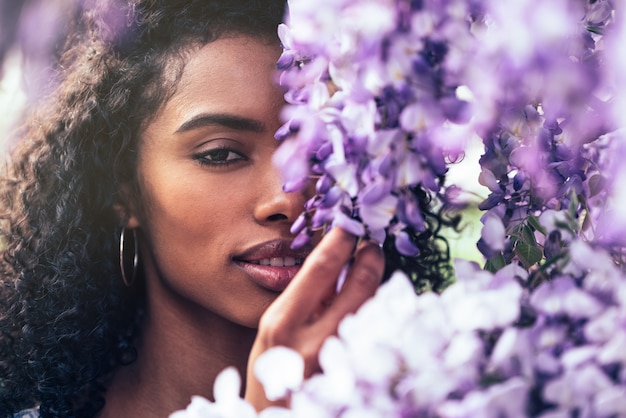 Réfléchie heureuse jeune femme noire entourée de fleurs