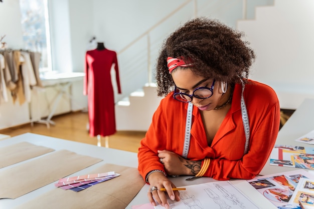 Réfléchir aux détails. Concentré de concepteur bouclé aux cheveux courts portant un crayon et à la recherche de croquis pendant le processus d'invitation