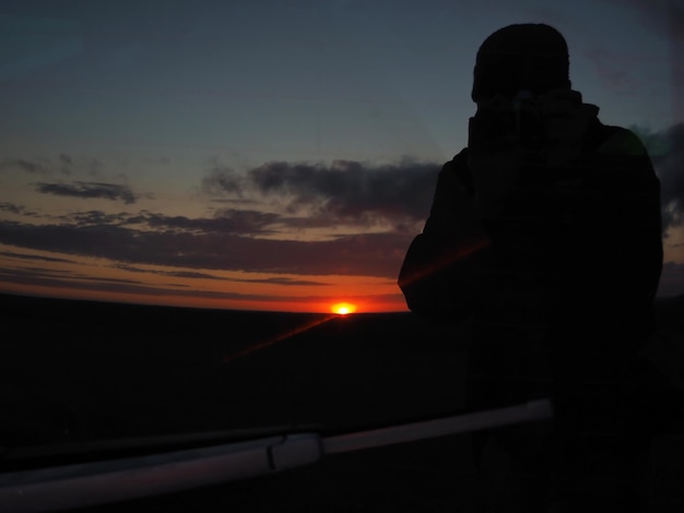 Photo reflet dans la lunette arrière d'un coucher de soleil coloré et de la silhouette d'un photographe.