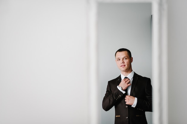 Reflet dans le miroir, l'homme en costume se regarde et redresse la cravate sur la chemise à la maison. concept de vêtements. préparation d'une réunion d'affaires.