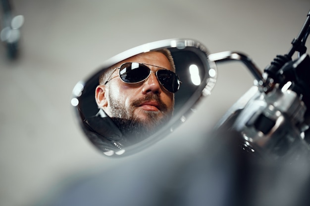 Reflet dans le miroir de moto d'un pilote homme à lunettes de soleil