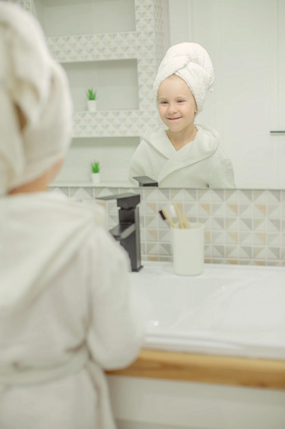 reflet dans le miroir de la salle de bain d'une fille dans une serviette blanche sur la tête et une robe blanche