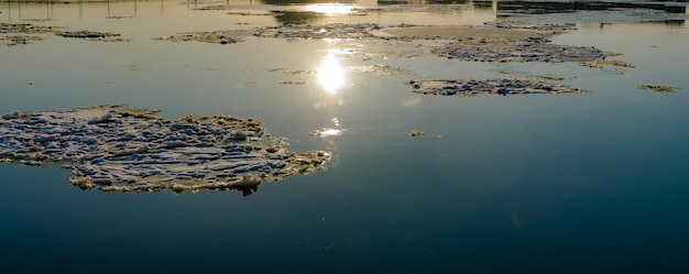 un reflet du soleil dans une rivière calme avec des morceaux de glace