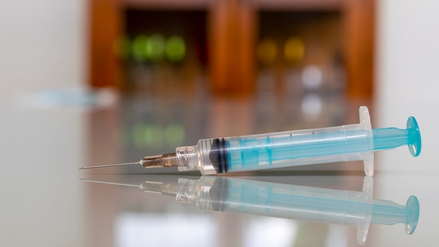 Reflet d'une seringue de vaccin sur une table en verre.