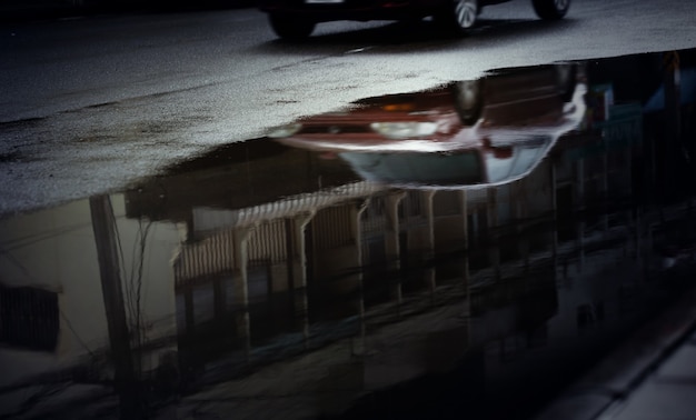 Reflet de voitures floues dans une flaque d'eau dans la rue de la ville après une forte pluie, mise au point sélective. Saison des pluies, arrière-plan des transports.