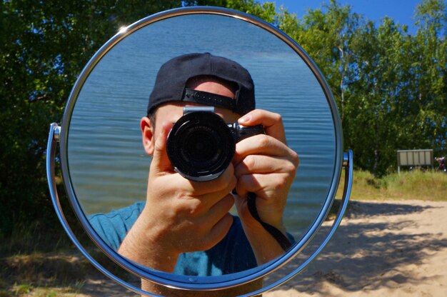 Photo réflexion d'un homme photographiant contre la mer avec un appareil photo numérique vu dans le miroir