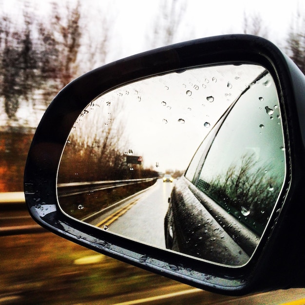 Photo réflexion d'une voiture sur la route vue à travers le miroir latéral pendant la mousson