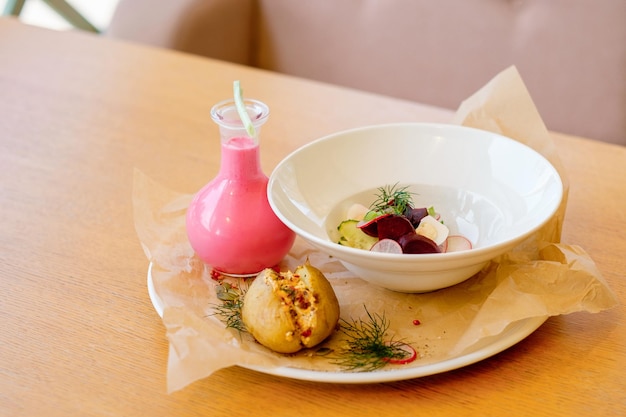 Réfrigérateur kéfir avec pomme de terre au four avec fromage cottage La soupe que l'invité se remplit Assiette blanche profonde avec des légumes et une bouteille avec vinaigrette rose Vue de dessus