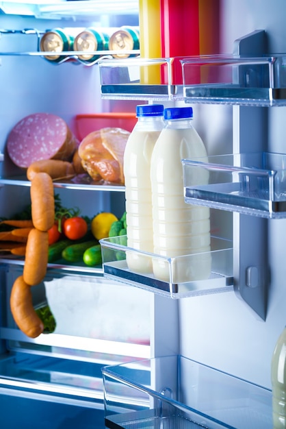 Réfrigérateur ouvert rempli de nourriture. Zoom sur les bouteilles de lait au frigo