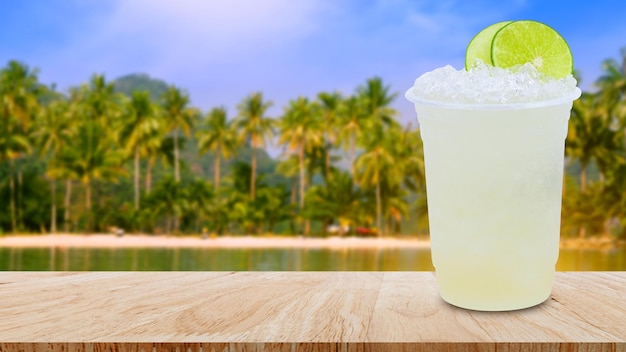 Refroidissez la limonade fraîchement préparée dans des gobelets en plastique avec de la glace pilée et des tranches de citron sur une table en bois avec fond nature paysage de plage