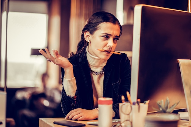 Regard énigmatique. Personne de sexe féminin concentrée regardant son ordinateur tout en accomplissant la tâche