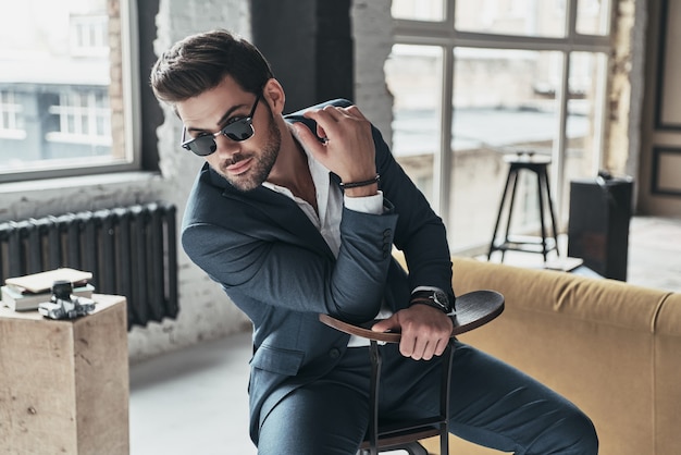 Regard incroyable! Beau jeune homme en costume complet à l'écart alors qu'il était assis sur le tabouret