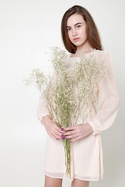 Regard romantique bouclé, beaux yeux. Fleurs sauvages blanches dans les mains. Fille robe légère blanche et cheveux bouclés, portrait de femme avec des fleurs sur fond blanc, pureté et innocence