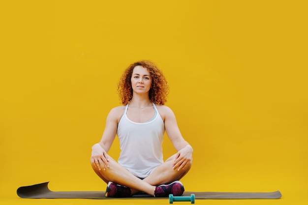 Regardant la caméra jeune femme assise les jambes croisées dans la pose de méditation de yoga