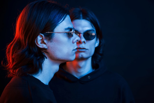 Regardant de face et de côté. Portrait de frères jumeaux. Studio tourné en studio sombre avec néon